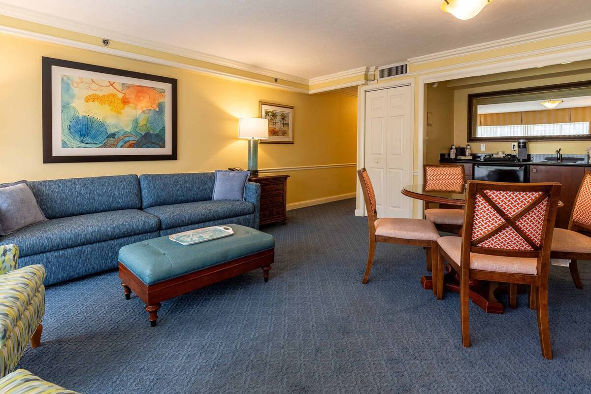 A living room with a blue sofa, a wooden coffee table, and a dining area with wooden chairs and a table.