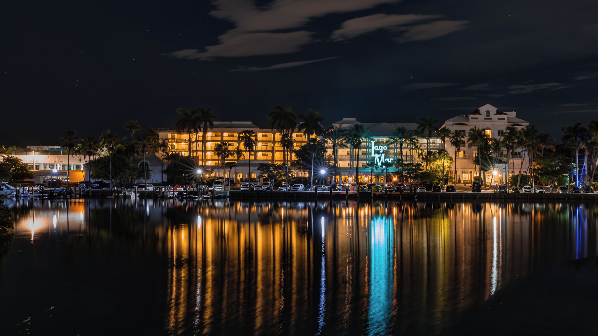 A waterfront hotel with multiple buildings, palm trees, and a calm lake reflecting the lights.