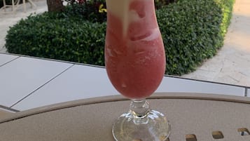 A drink in a glass with a straw, placed on a table with a view of palm trees and a patio area.