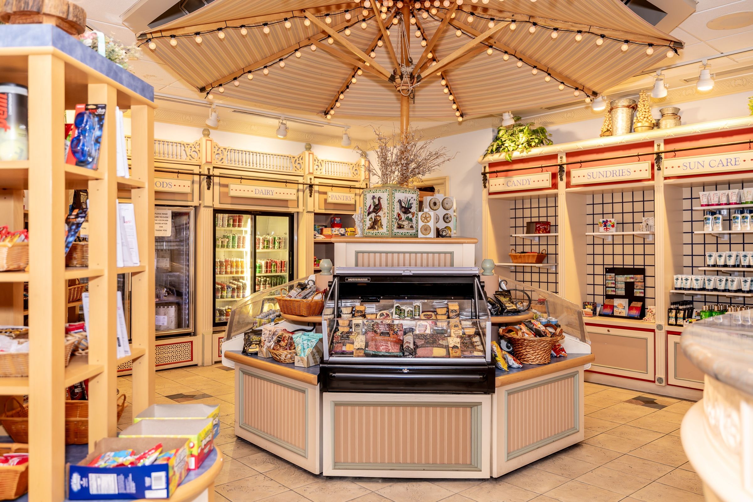 A store interior with a central display case, refrigerated sections, and shelves labeled with product categories like 'CANDY' and 'SUN CARE'.