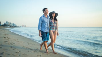 Um casal caminhando na praia, com o horizonte da cidade ao fundo.