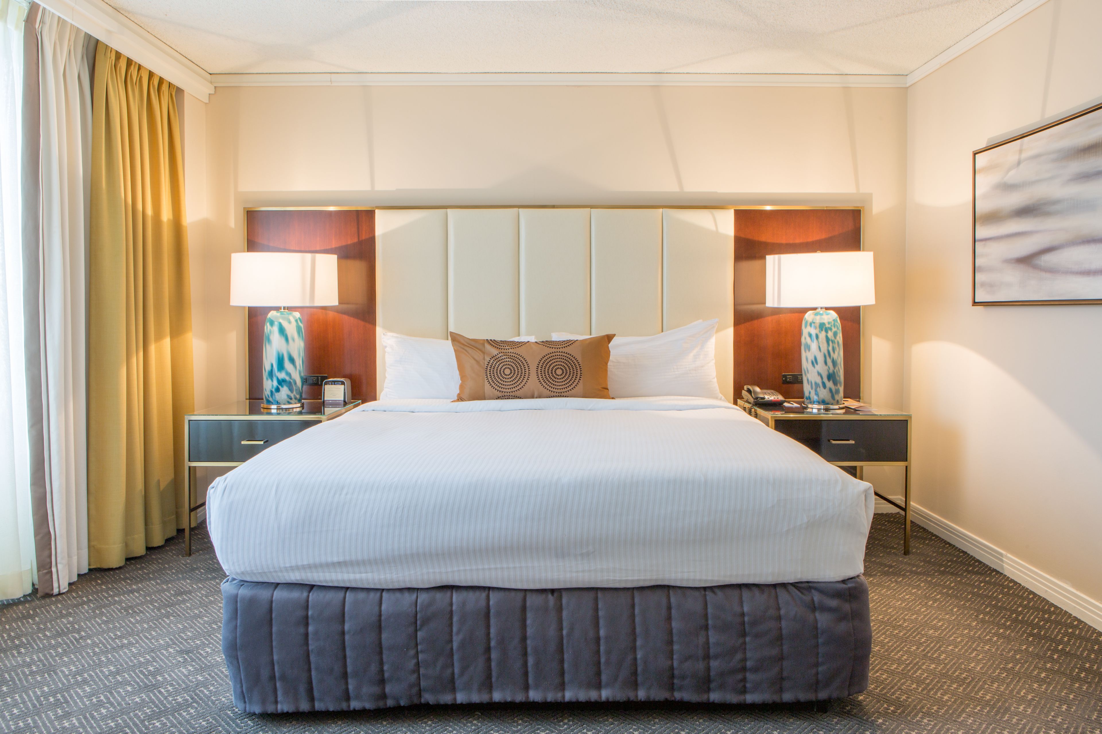 A hotel room with a large bed, two bedside tables with lamps, a headboard, and a painting on the wall.