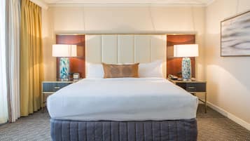 Una habitación de hotel con una cama grande, dos mesitas de noche con lámparas, un cabecero y un cuadro en la pared.