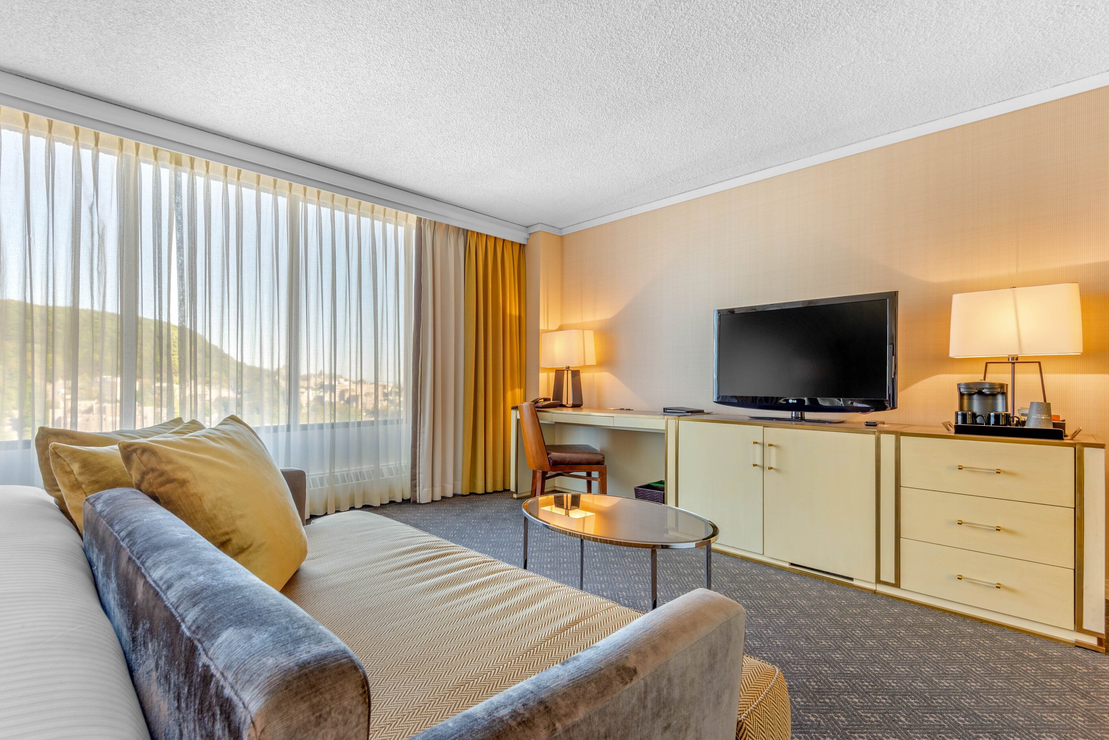 A hotel room with a bed, a sofa, a desk with a TV, and a minibar.