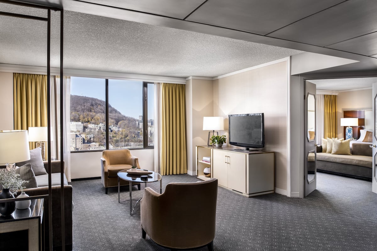 A hotel room with a large window, a television, a sofa, a chair, and a small table.