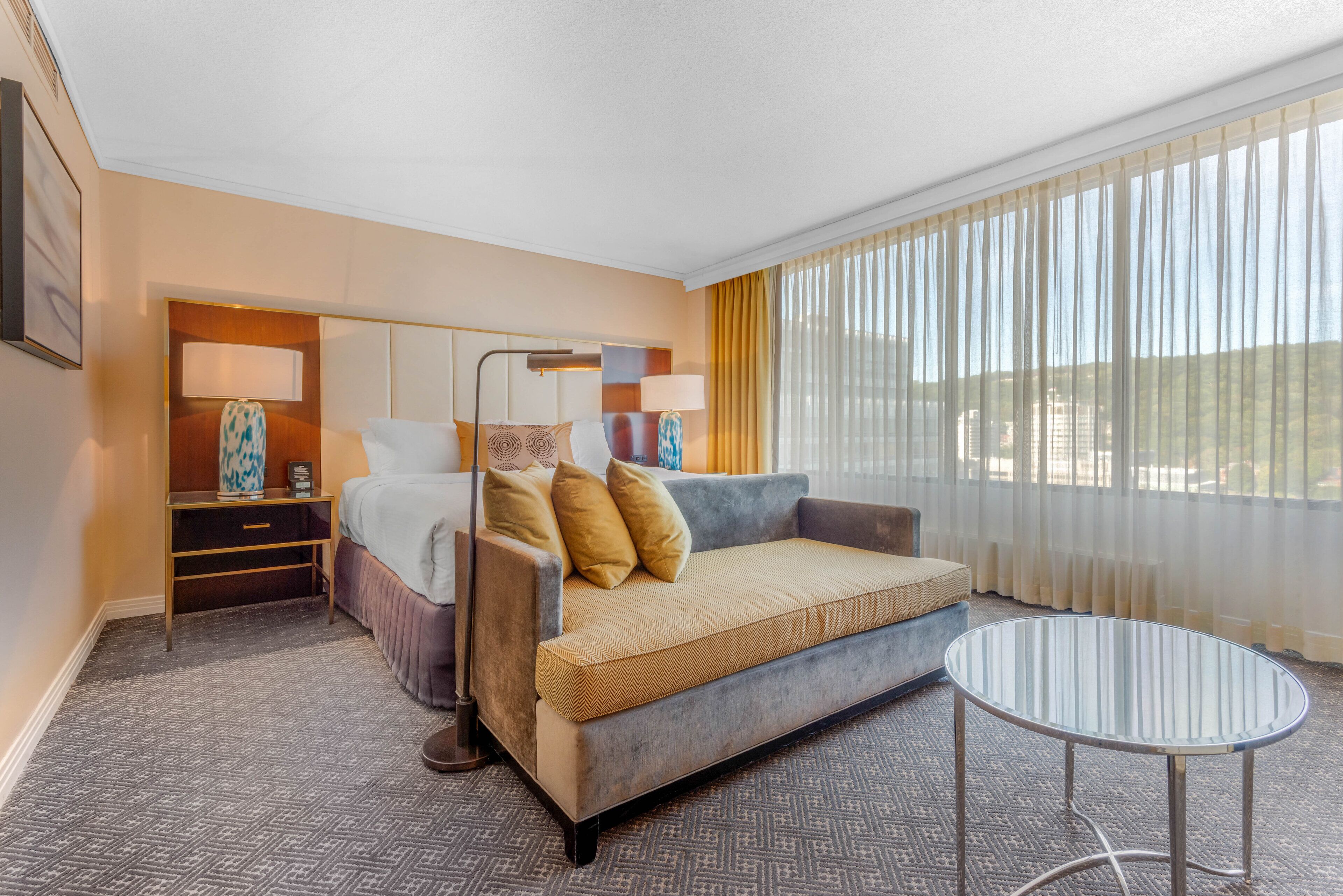 A hotel room with a bed, a sofa, a small table, and a window with curtains.