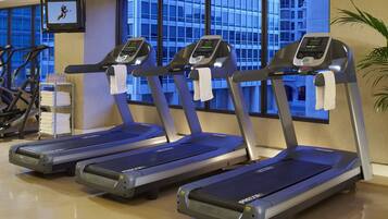 Three treadmills in a gym with a view of a building through large windows.