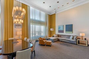 Une chambre d’hôtel avec une grande table ronde, un canapé, une table basse et un lustre.