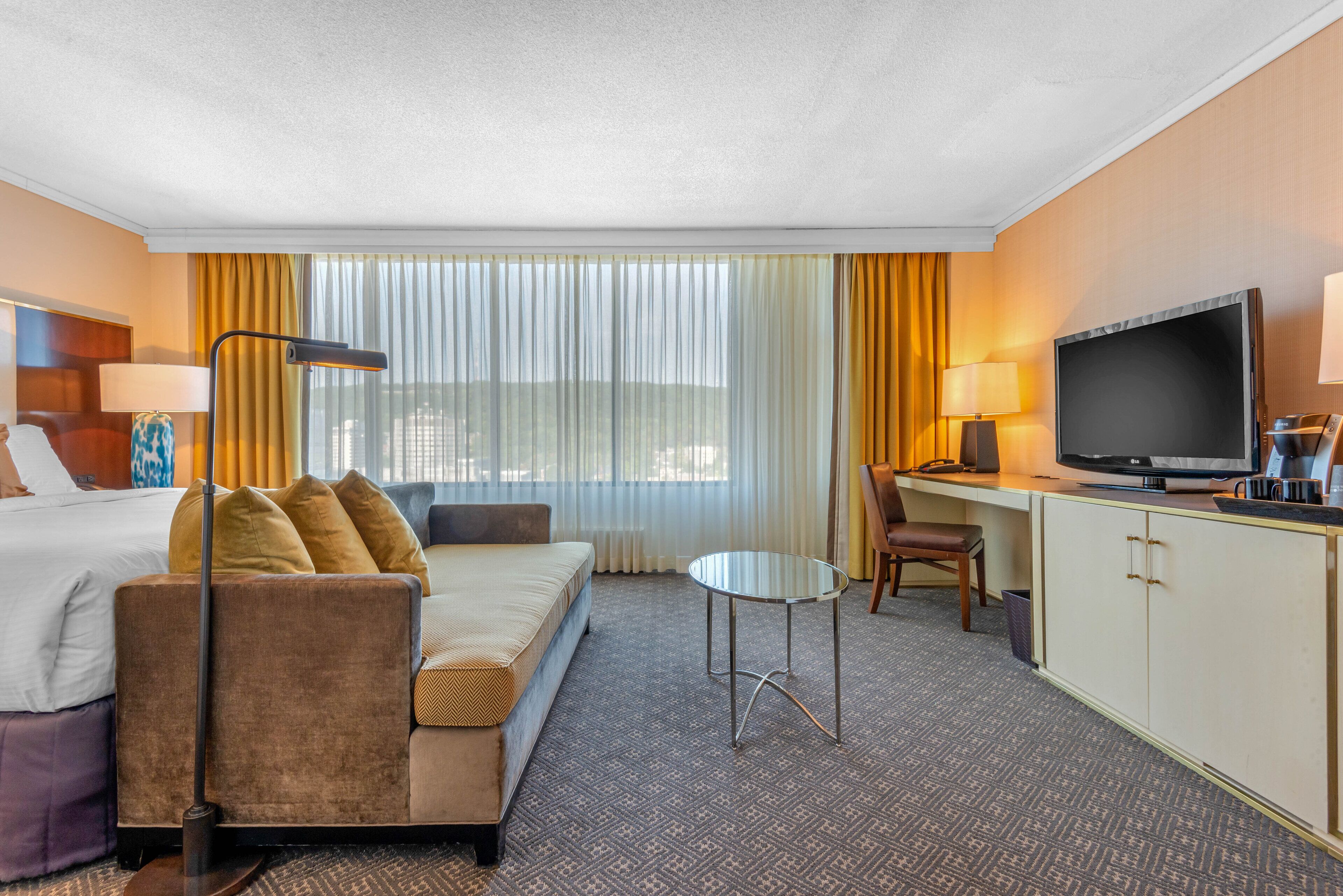 Ein Hotelzimmer mit einem Bett, einem Schlafsofa, einem Schreibtisch, einem Fernseher und einem Fenster mit Vorhängen.