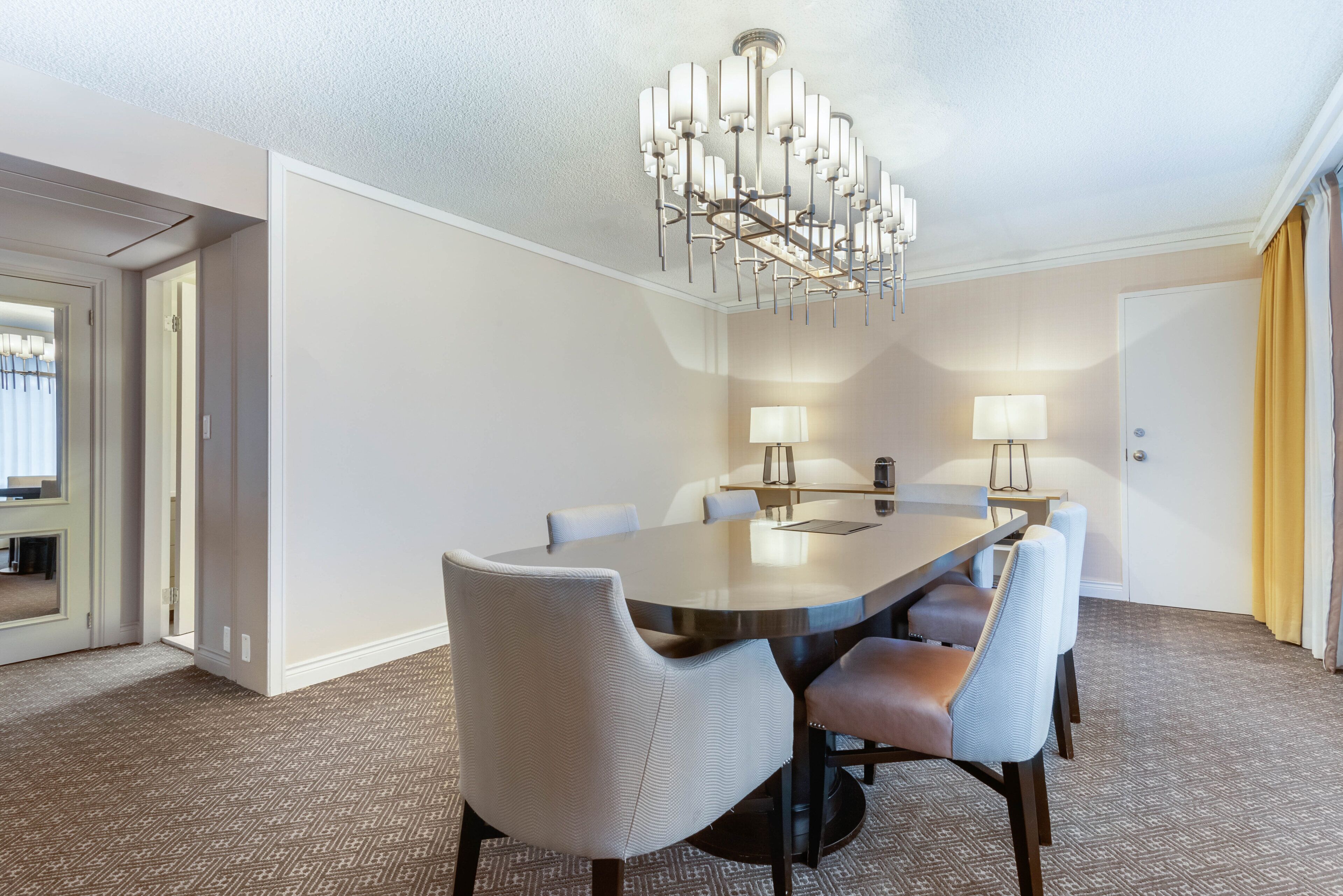 Une salle à manger d’hôtel avec une table ronde, six chaises, deux lampes fixées au mur et un lustre.