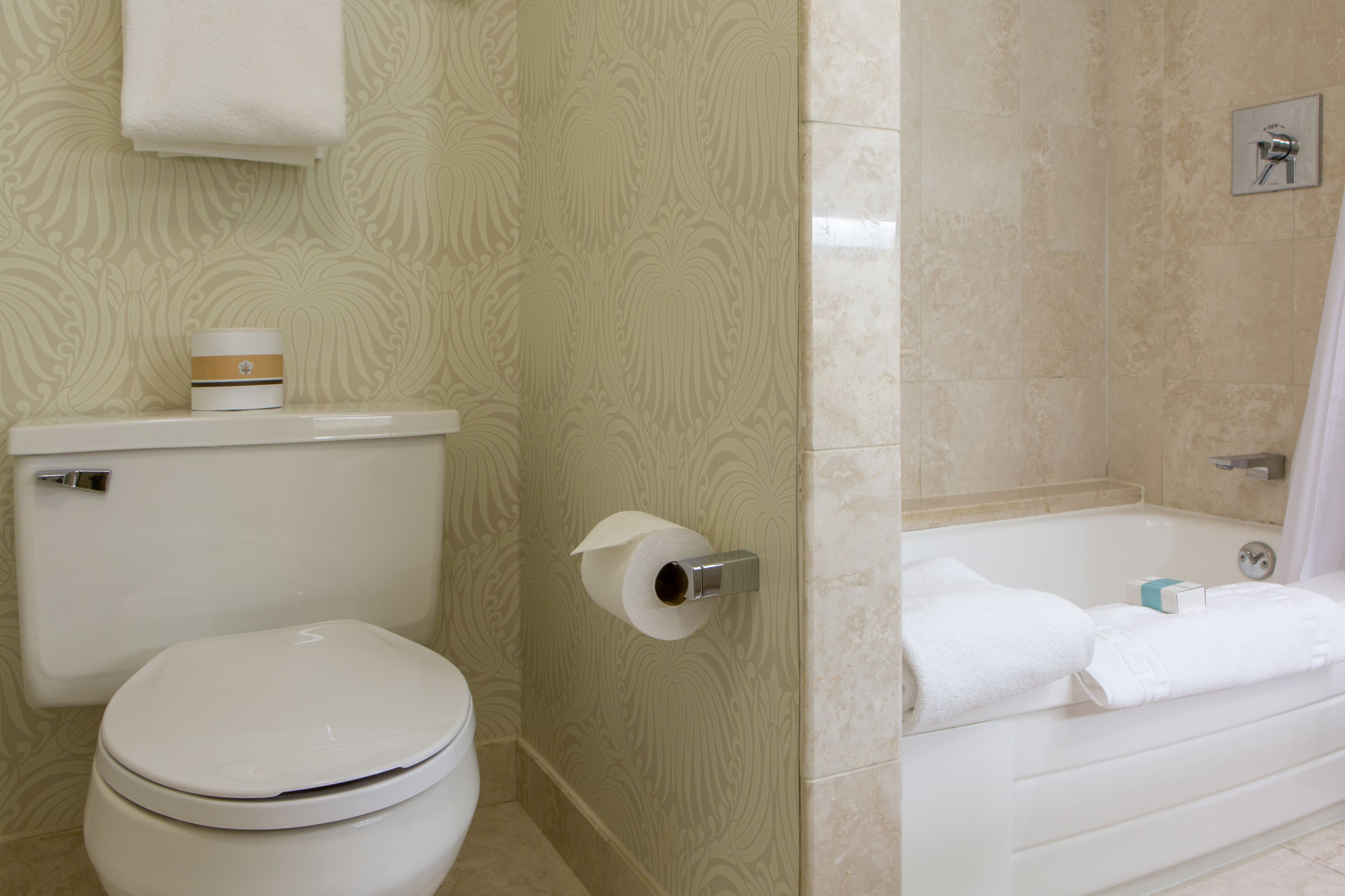 Un baño con inodoro, dispensador de papel higiénico y bañera con toallas.