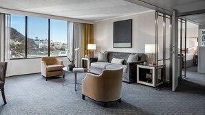 A modern hotel room with a large window, a sofa, a chair, and a small table.