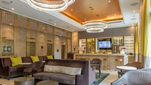 A modern hotel lobby with a bar area, seating arrangements, and a television screen.