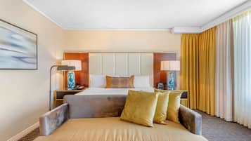 A hotel room with a large bed, two bedside tables with lamps, a sofa, and a large window with curtains.
