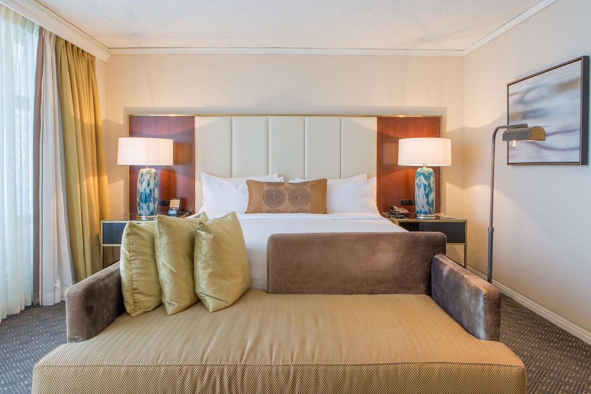 A hotel room with a large bed, two bedside tables with lamps, a sofa, and a painting on the wall.