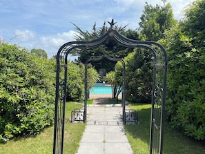 Un sendero de jardín que lleva a una zona de piscina con un arco de metal.