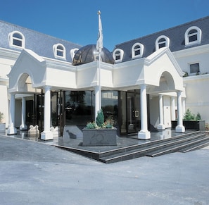 Entrada de hotel con vestíbulo cubierto, columnas y un elemento decorativo central.
