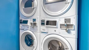 A multi-unit commercial washing machine with control panels and a blue wall background. - Days Inn & Suites by Wyndham Albuquerque North (Albuquerque)