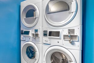 Lavadora industrial con varios tambores, paneles de control y un fondo de pared azul.