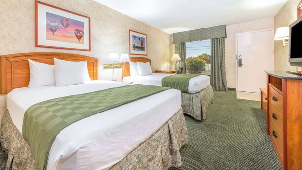 A hotel room with two beds, a TV, a desk, and a window with curtains. - Days Inn & Suites by Wyndham Albuquerque North (Albuquerque)