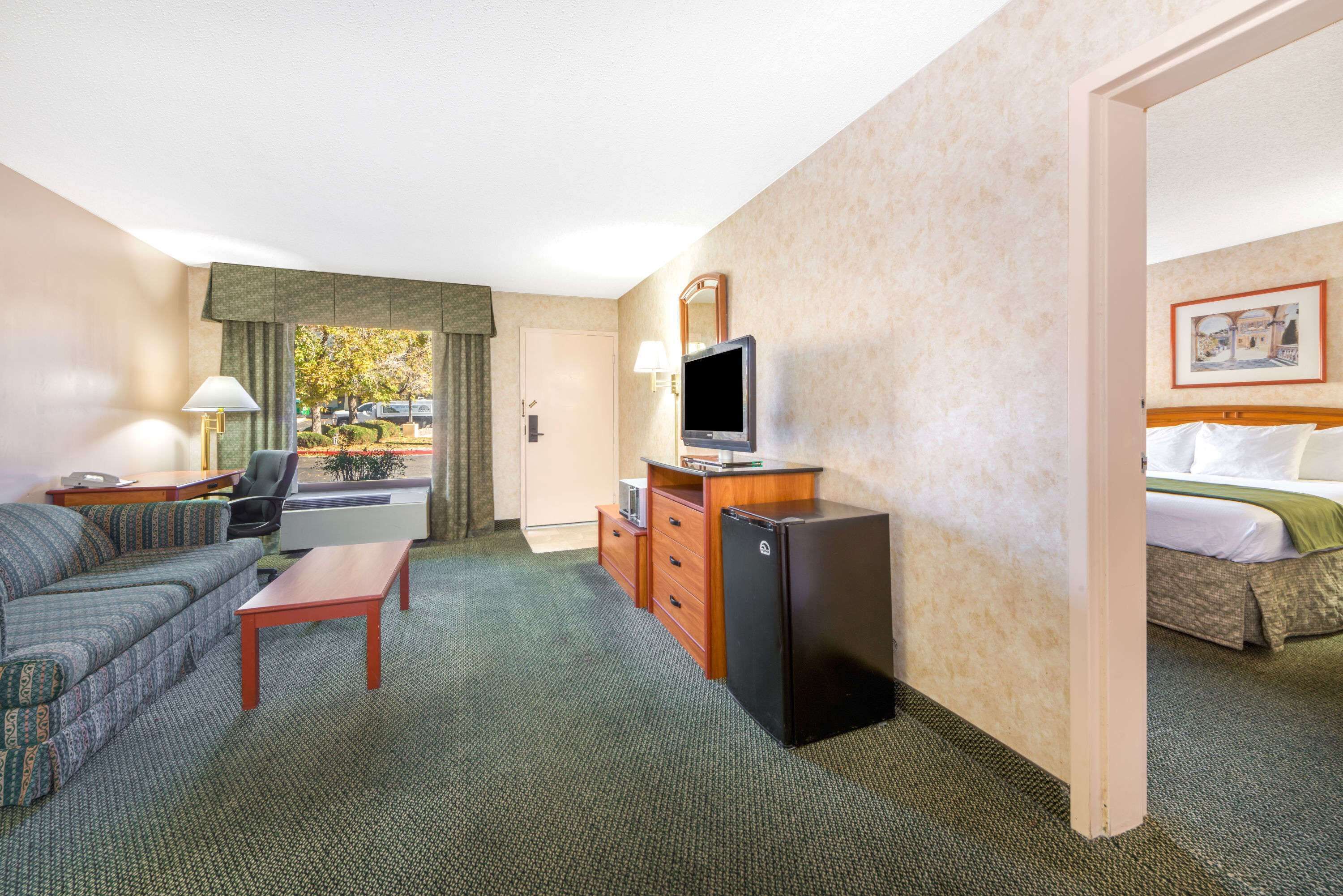 A hotel room with a sofa, a desk, a television, a refrigerator, and a bed.