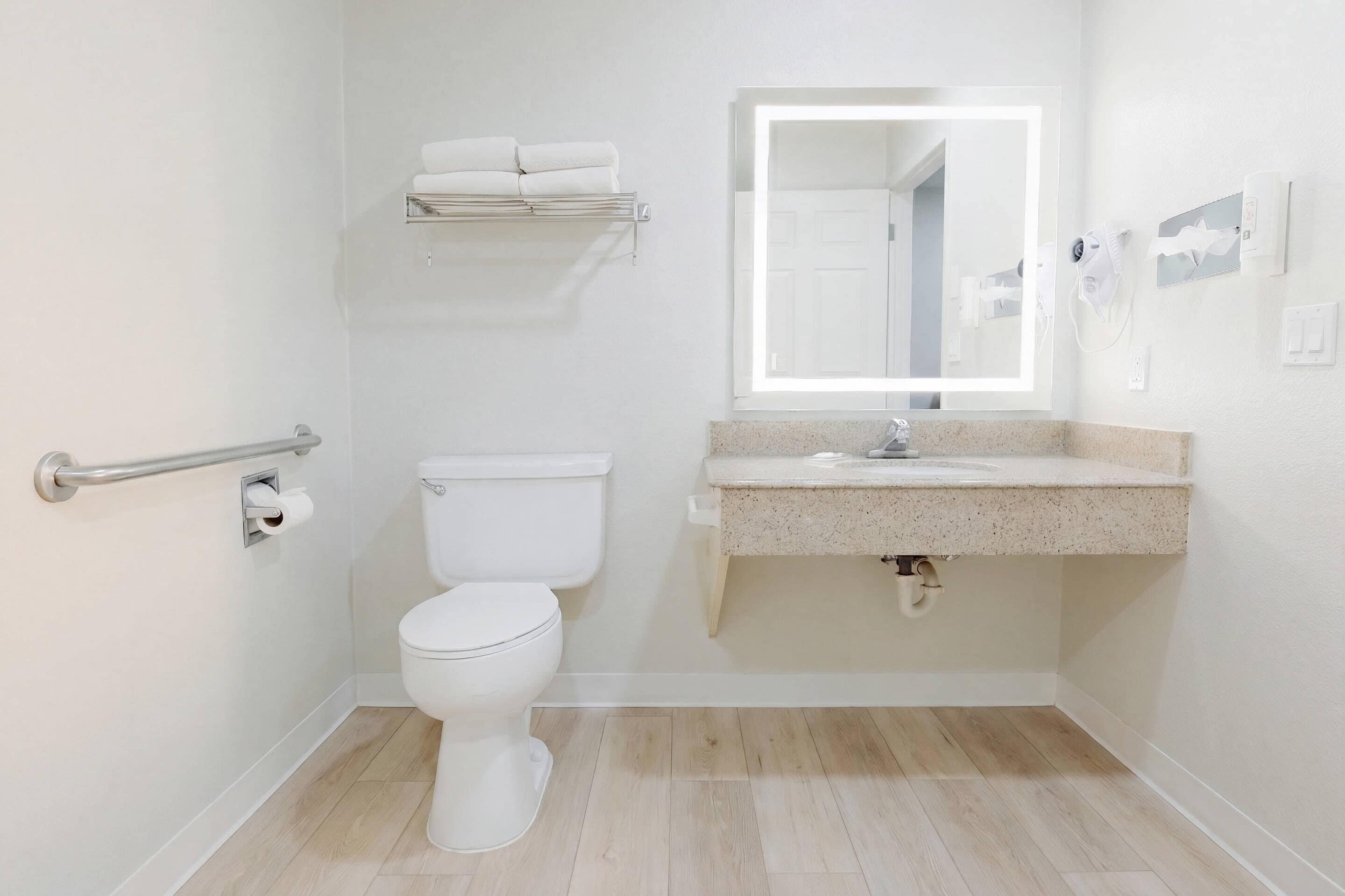 Un baño con inodoro, lavamanos, espejo y toallero.