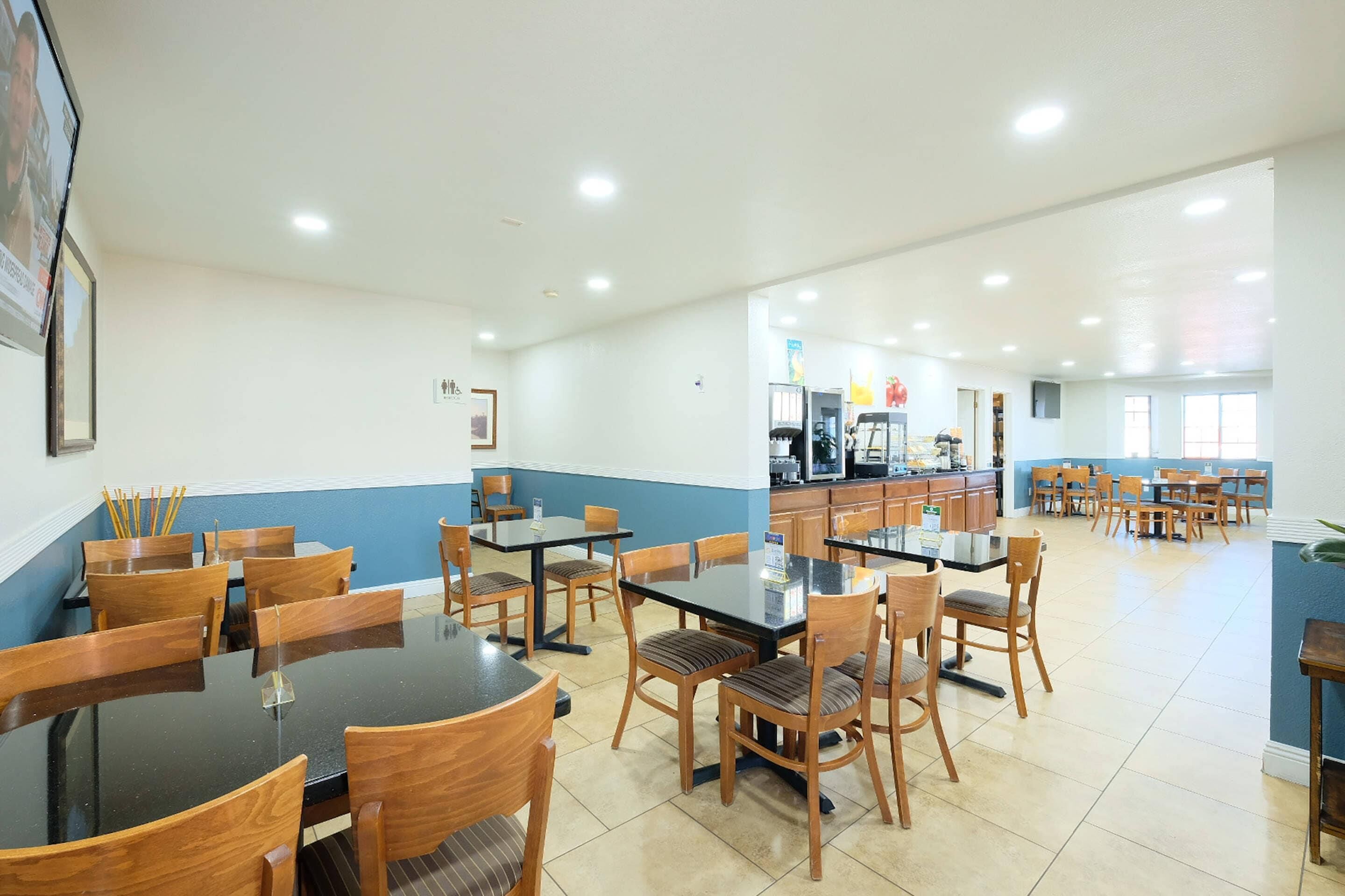 A spacious dining area with multiple tables and chairs, a kitchen in the background, and a blue and white color scheme.