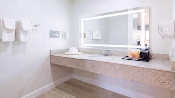 A modern bathroom with a granite countertop, a large mirror, a towel rack, and a hairdryer.