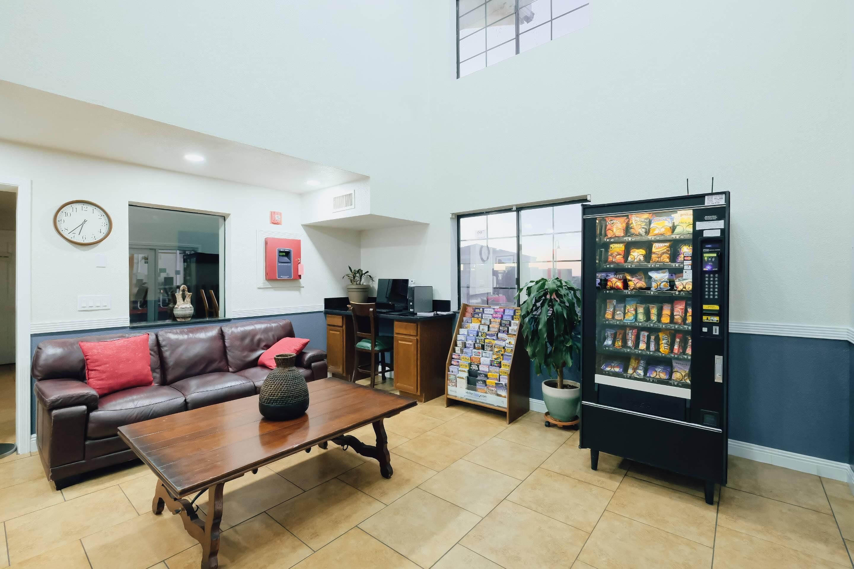 A lobby with a leather sofa, a wooden table, a vending machine, a computer desk, and a clock on the wall.