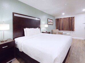 A hotel room with a large bed, a bedside table with a lamp, a chair, and a window with curtains. - Quality Inn Holbrook near Petrified Forest (Holbrook)