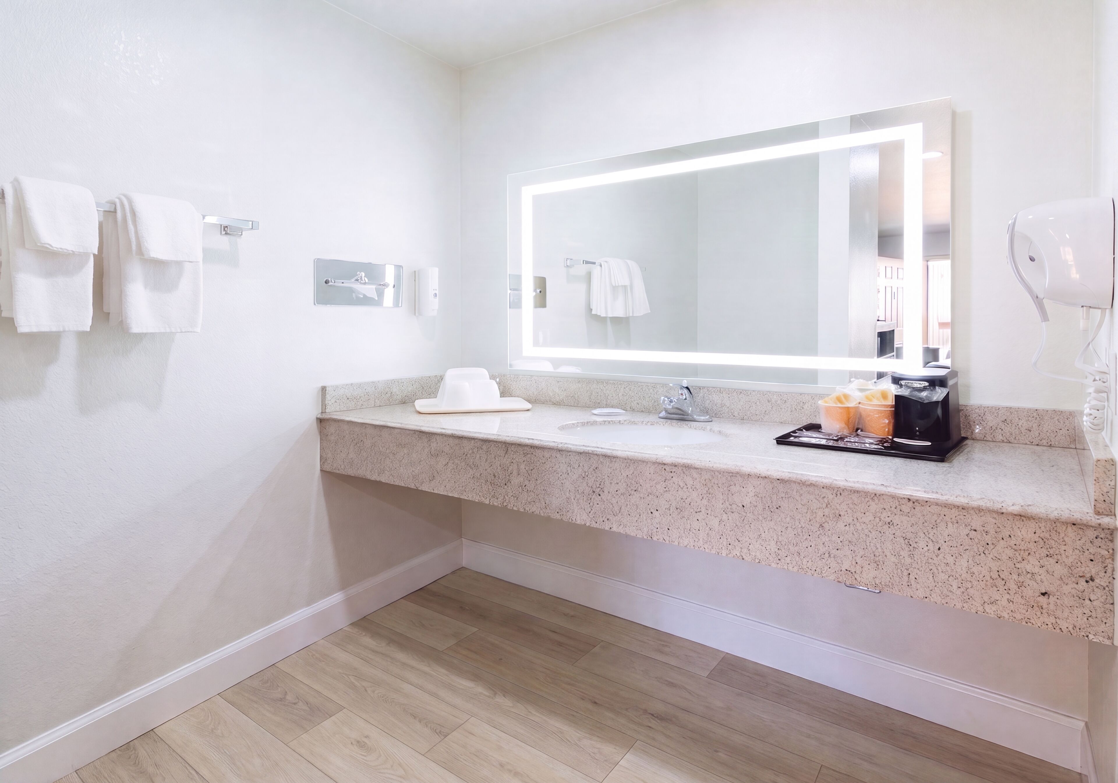 A modern bathroom with a granite countertop, a large mirror, a hairdryer, and a towel rack.