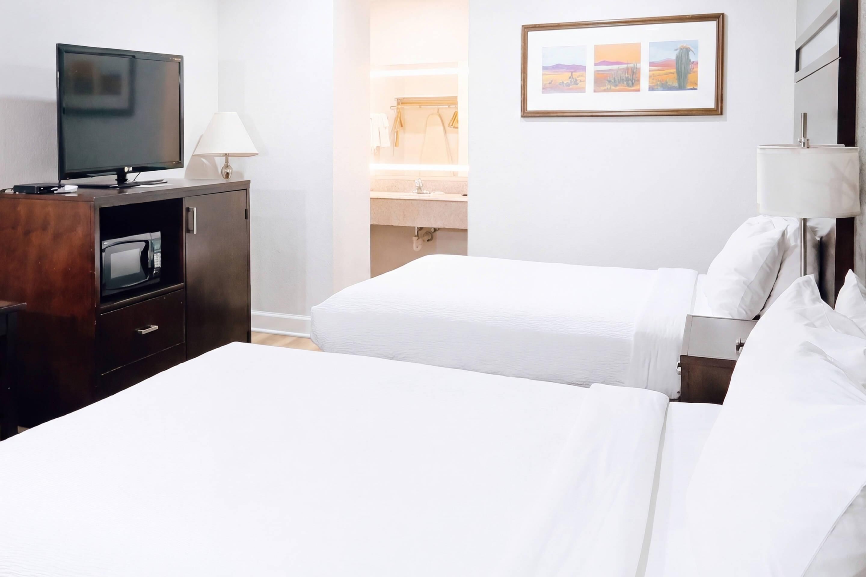 Une chambre d’hôtel avec un lit, une télévision, un bureau avec une lampe, une salle de bain et un tableau encadré au mur.