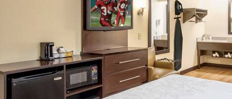 A hotel room with a bed, a television mounted on the wall, a desk with a coffee maker, a microwave, and a mirror.