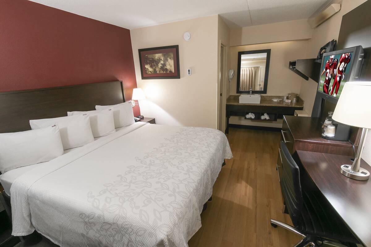 A hotel room with a large bed, a desk with a lamp, a mirror, and a TV on the desk.
