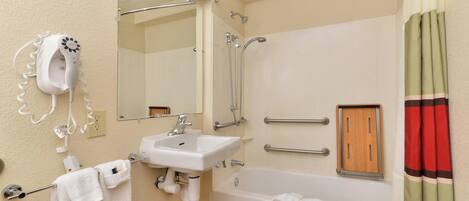 Un baño con un lavabo blanco, un espejo, un secador de pelo portátil, una ducha con puerta de vidrio y una bañera.
