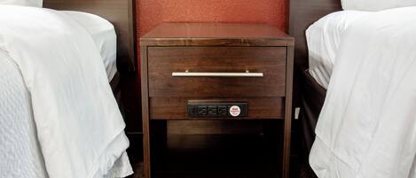 A wooden bedside table with a drawer and a plug-in socket, positioned between two beds with white linens.