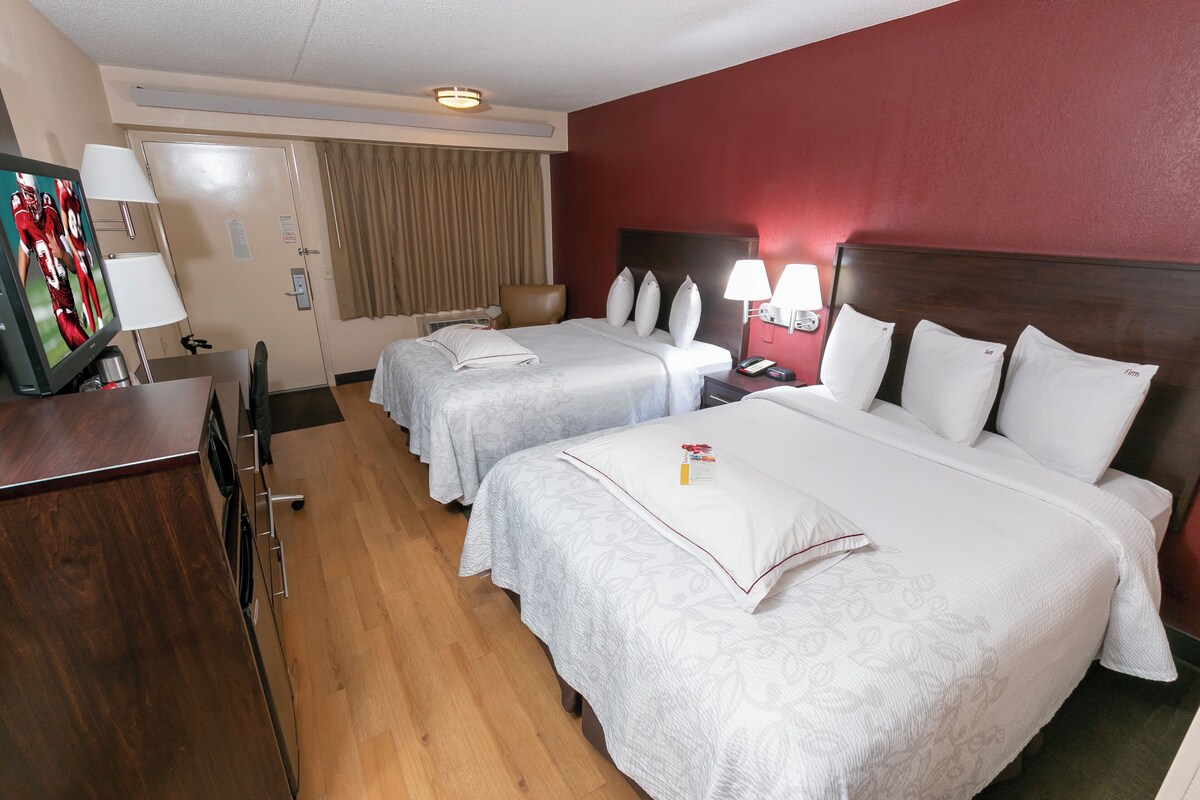 Una habitación de hotel con dos camas, un escritorio, un televisor y una ventana con cortinas.