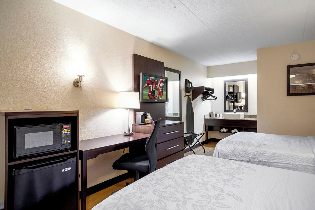 Habitación de hotel con cama, escritorio con computadora, microondas, refrigerador, espejo y ventana.