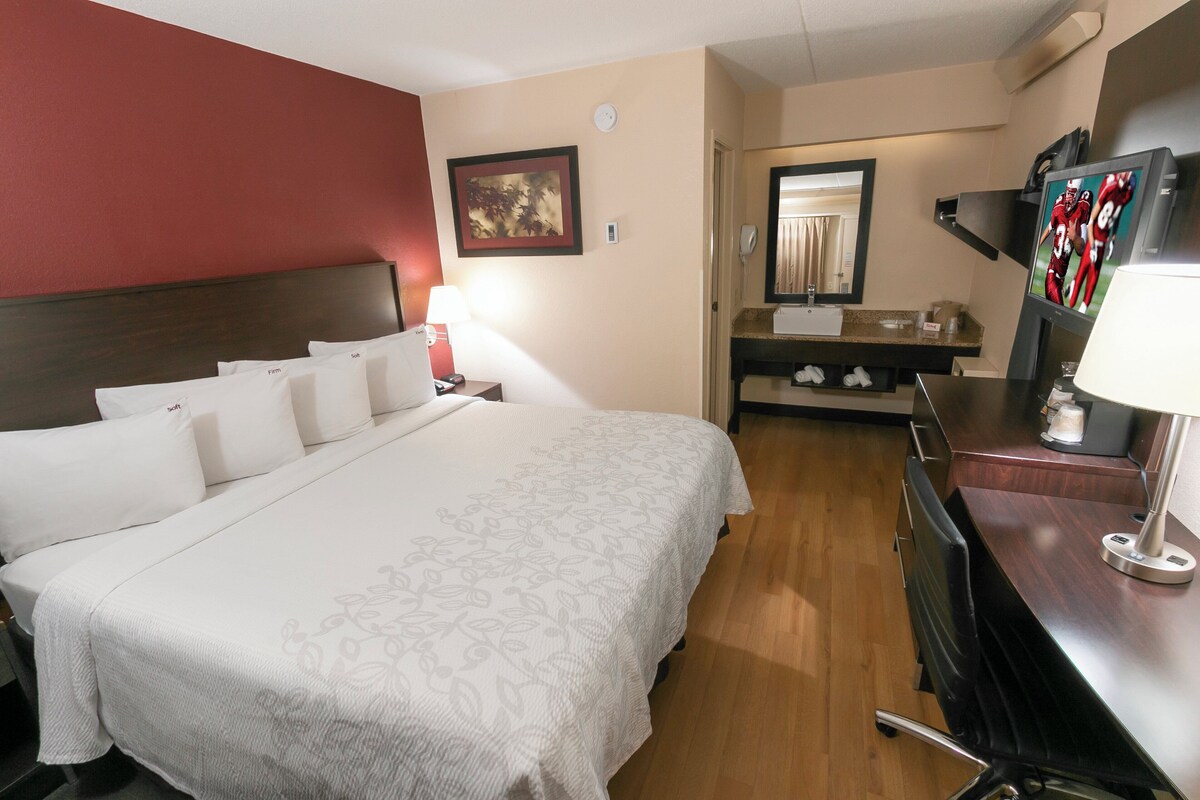Habitación de hotel con cama, escritorio, espejo, televisión y baño.