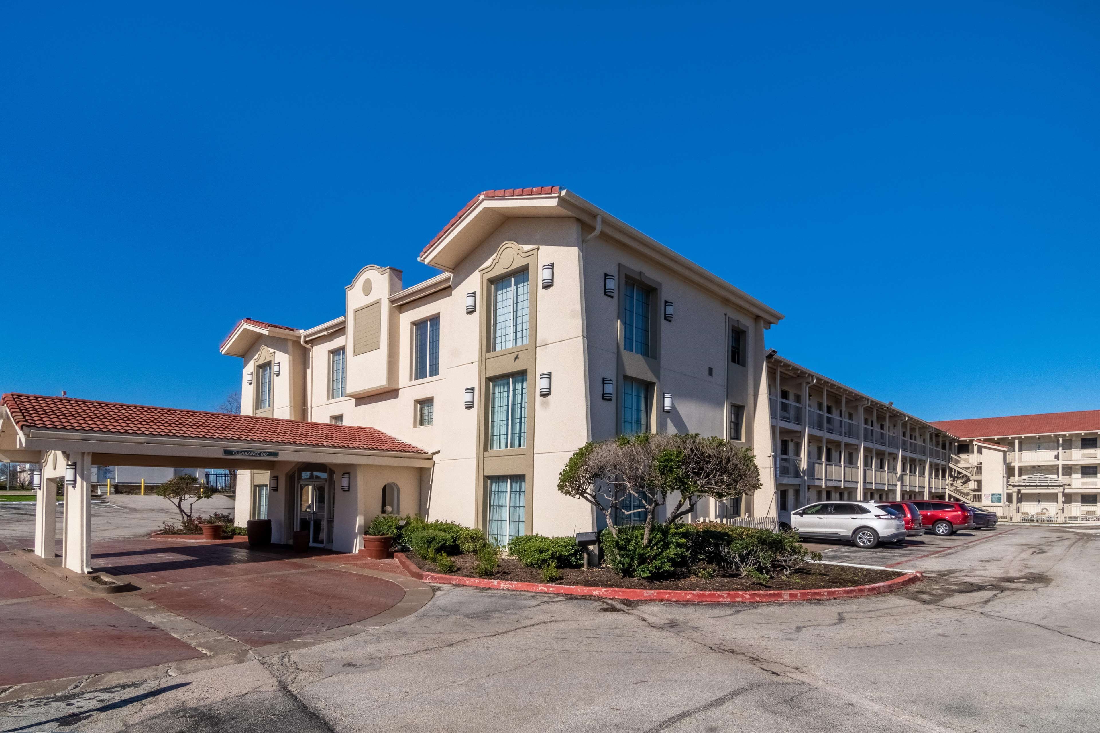A multi-story hotel with a covered entrance, a parking lot, and a clear blue sky.
