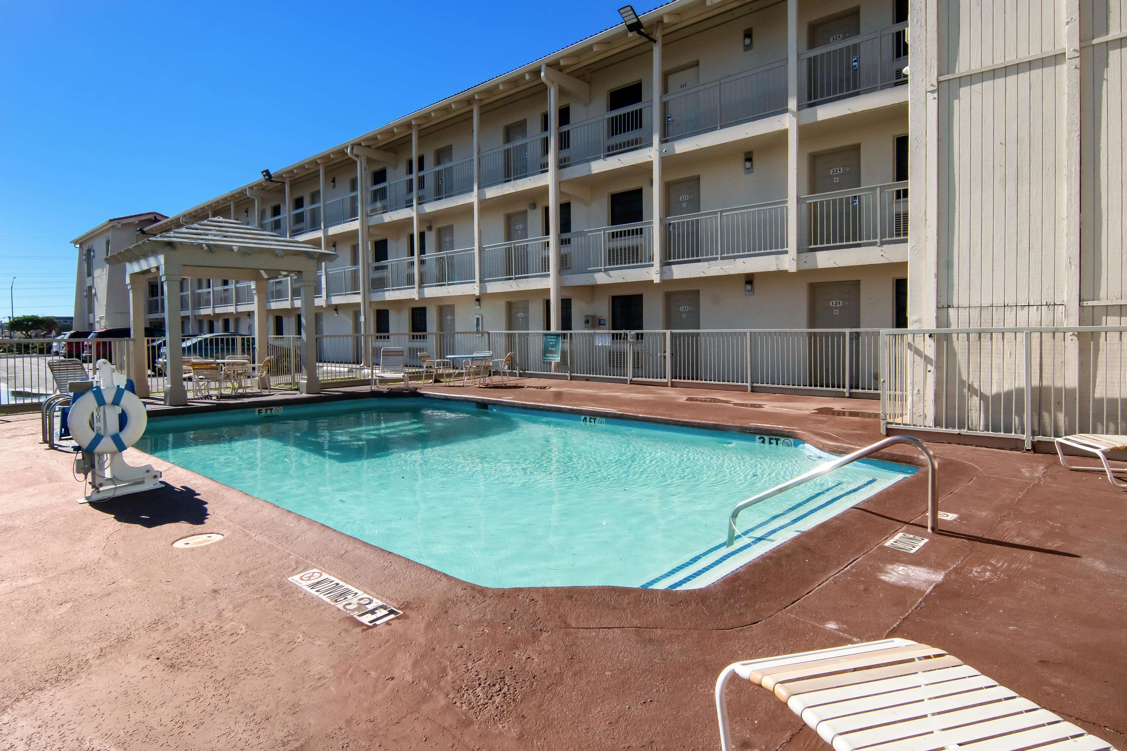 Un motel de varios pisos con piscina, área de estar al aire libre y puesto de socorrista.