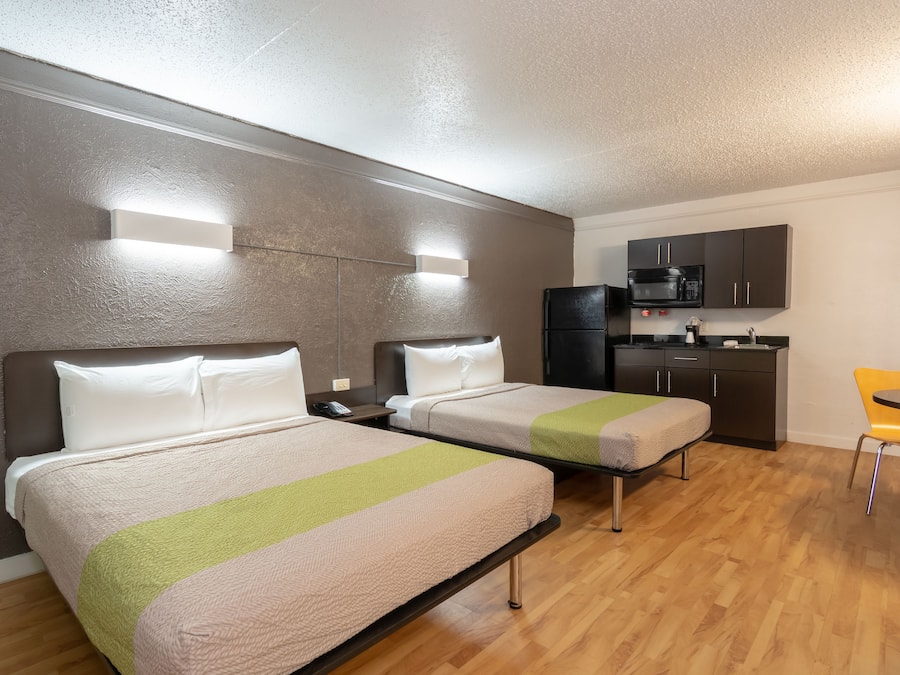 Quarto de hotel com duas camas, cozinha compacta e área de refeições.