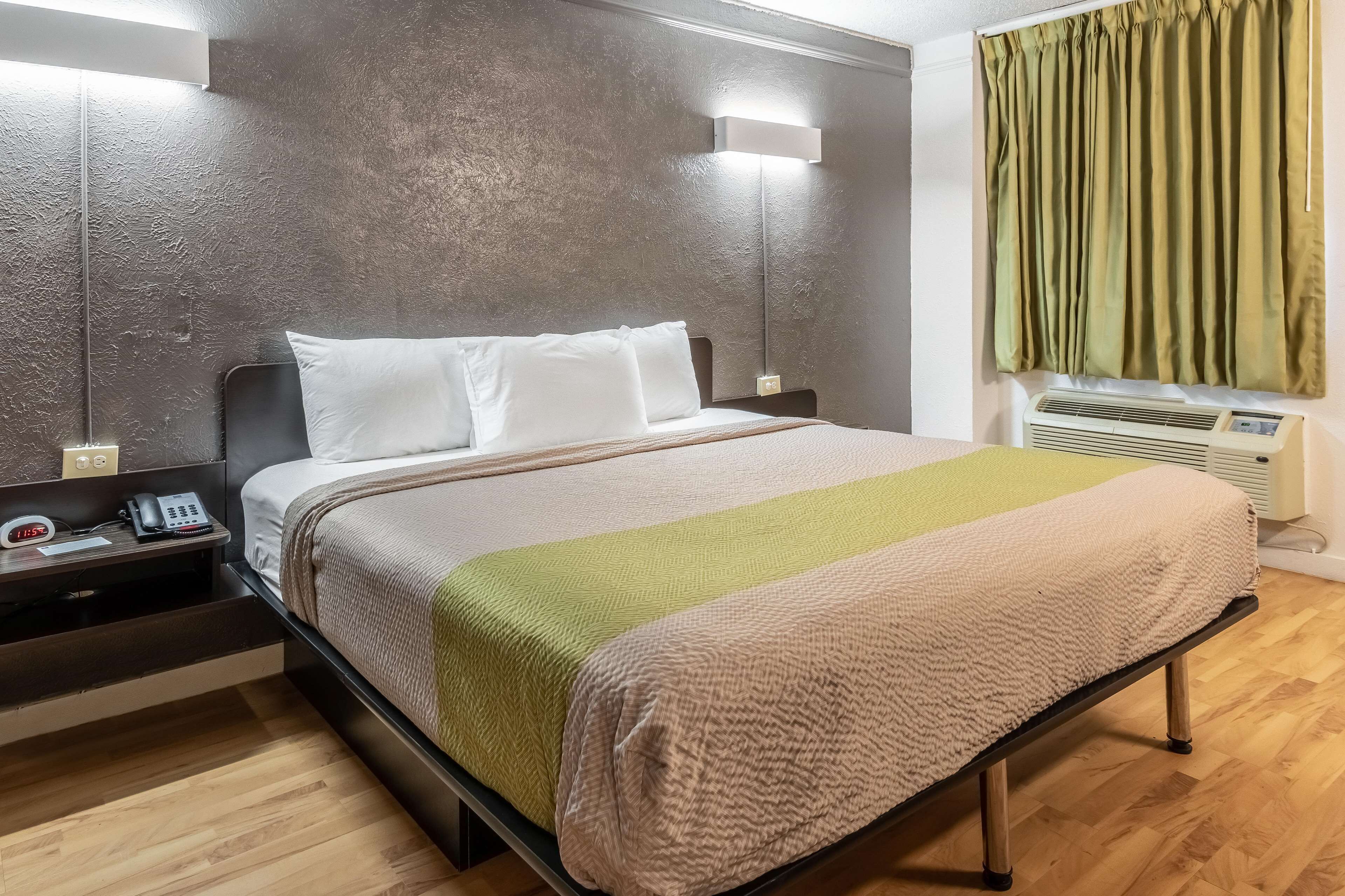 A modern hotel room with a large bed, bedside table with a phone, and a wall-mounted air conditioner.