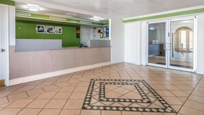 A reception area with a green wall, a reception desk, and a patterned floor. - Studio 6 Fort Worth, TX - West Medical Center (Fort Worth)