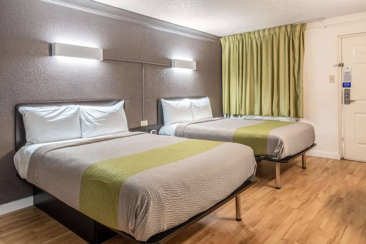 Habitación de hotel con dos camas, suelo de madera, cortina verde y una puerta con cerradura.