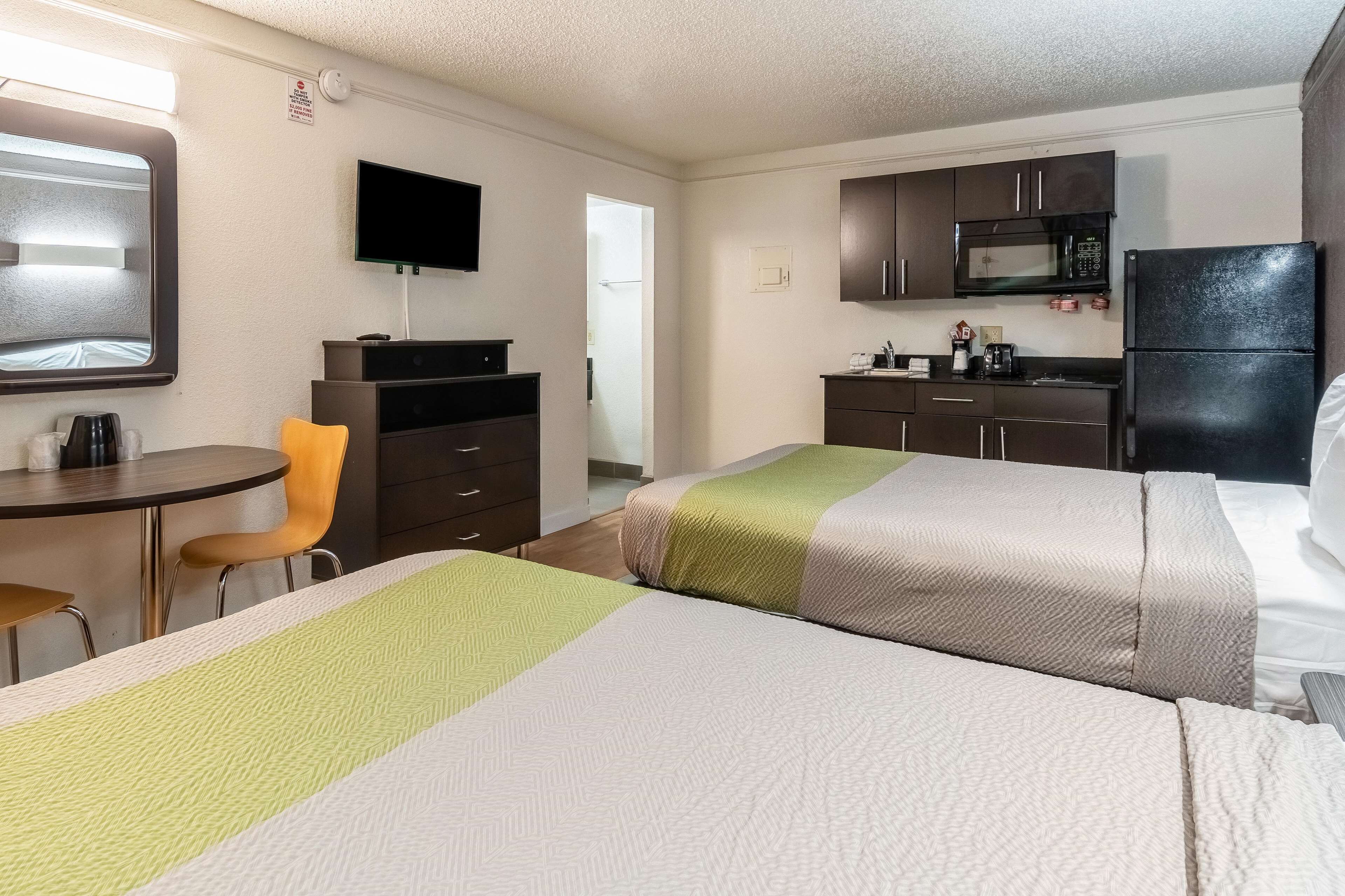 A hotel room with two beds, a desk with a chair, a TV, a microwave, and a refrigerator.