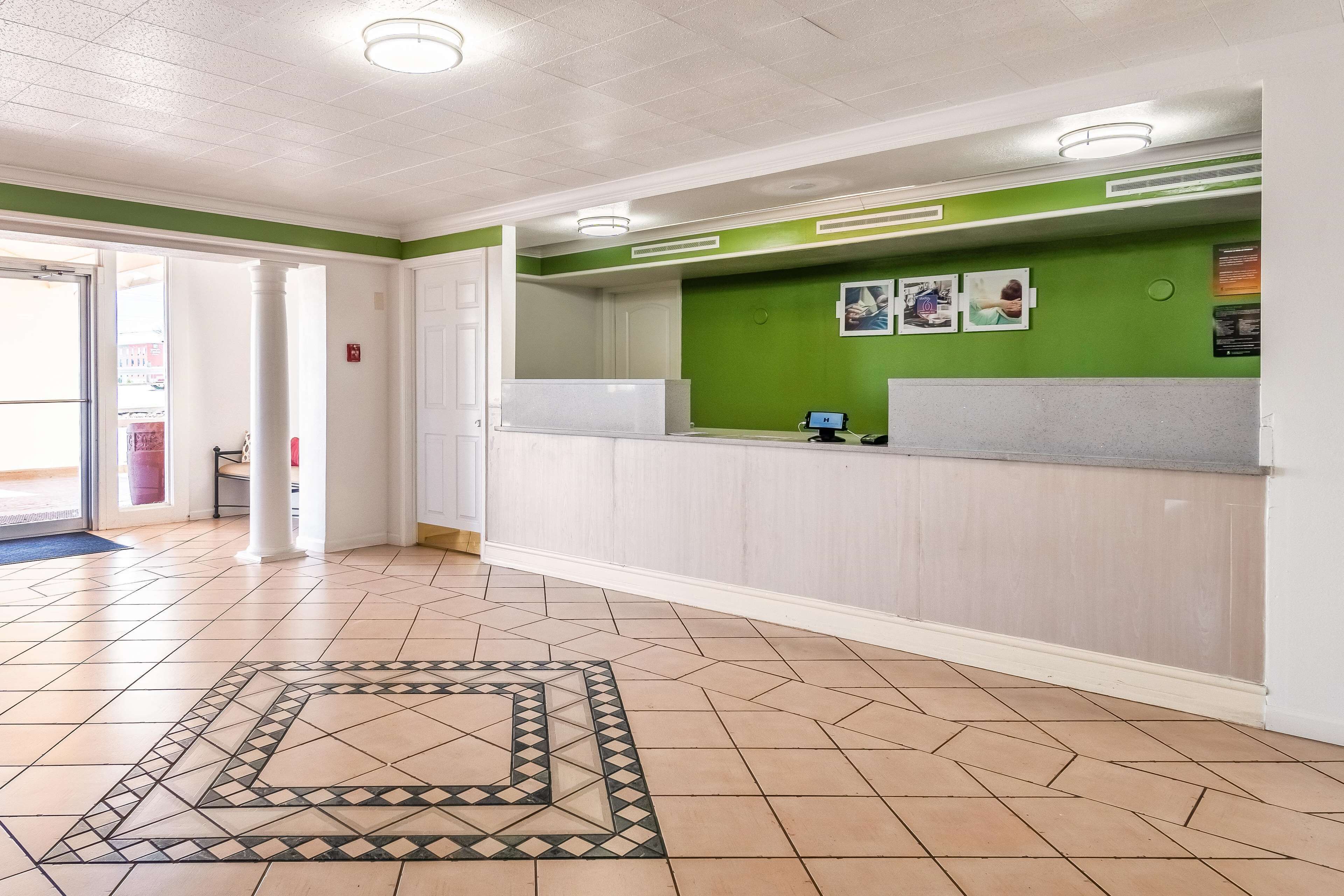 Een receptie met een groene wand, een wit receptiebalie en een vloer met een patroon.
