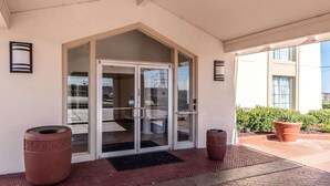 A hotel entrance with a glass door, two large potted plants, and a tiled walkway. - Studio 6 Fort Worth, TX - West Medical Center (Fort Worth)