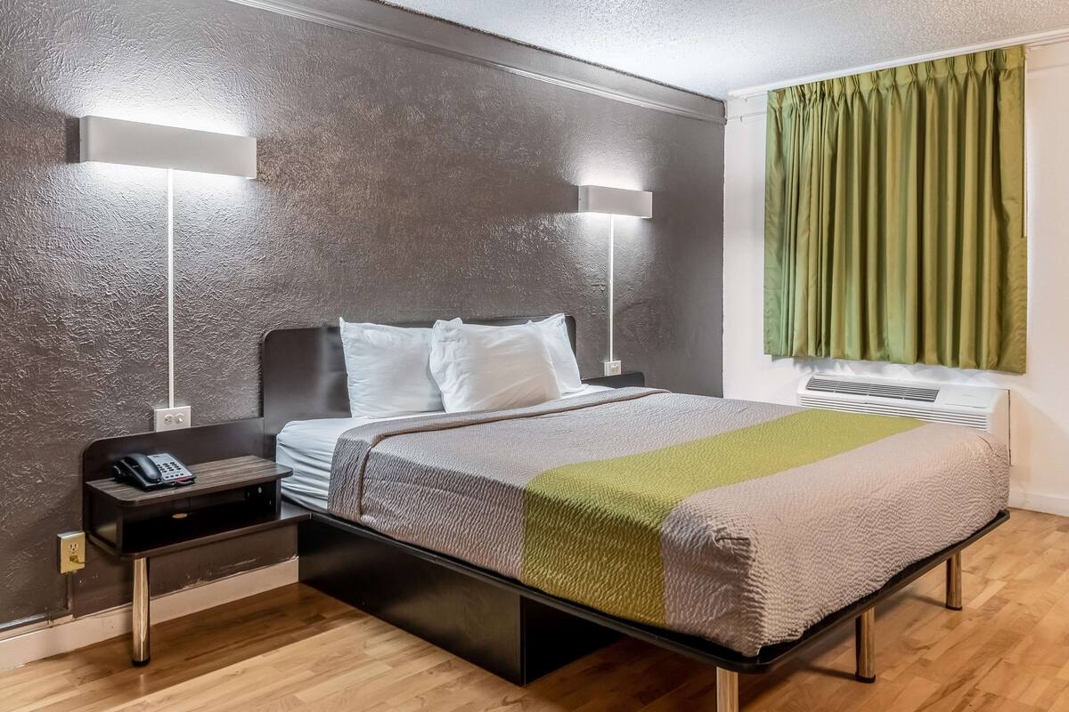 Una habitación de hotel moderna con una cama grande, lámparas de noche, una mesita de noche y una ventana con cortinas.