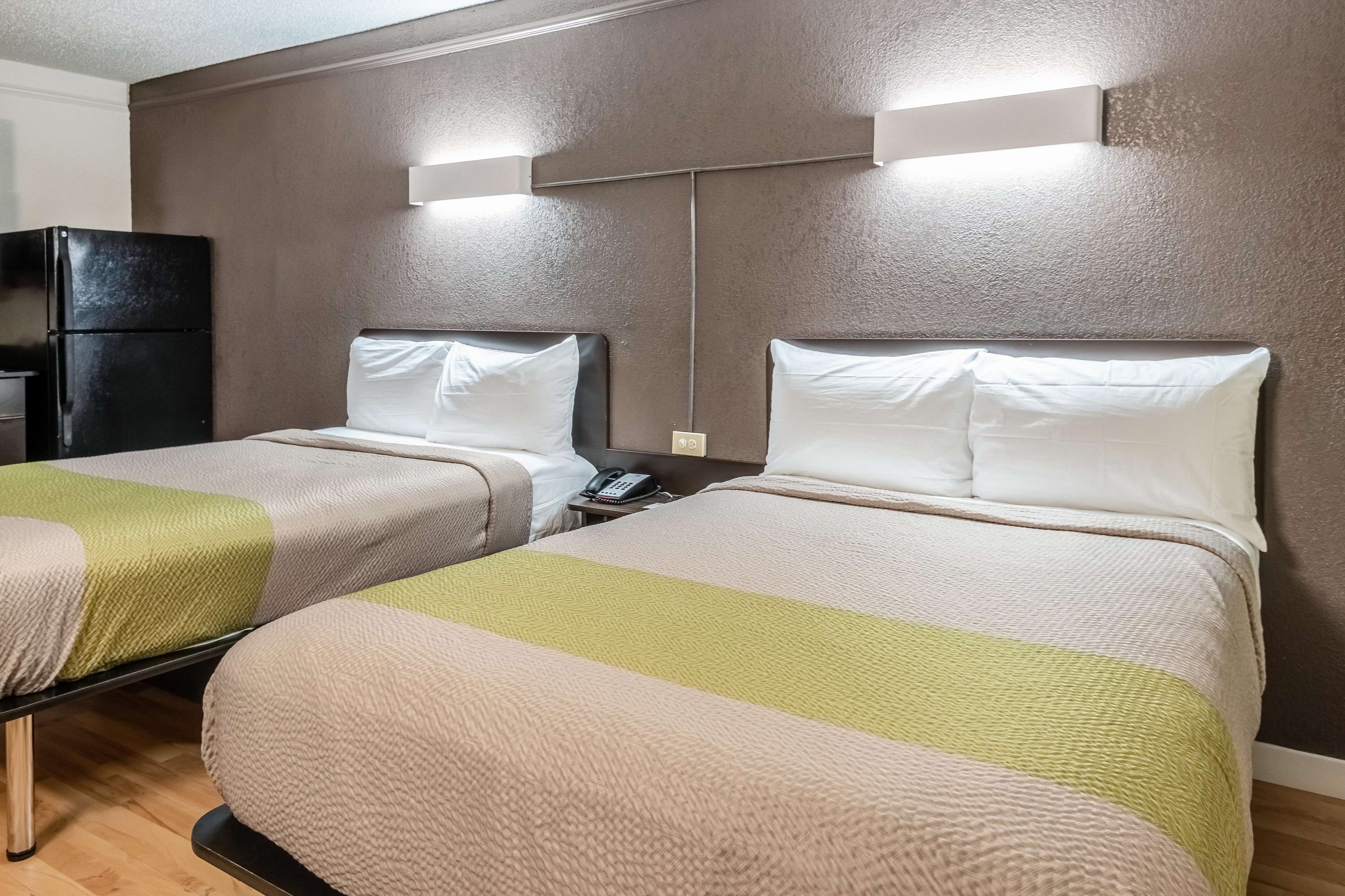 Habitación de hotel con dos camas, cada una con una manta verde y beige, un refrigerador negro y un teléfono junto a la cama.